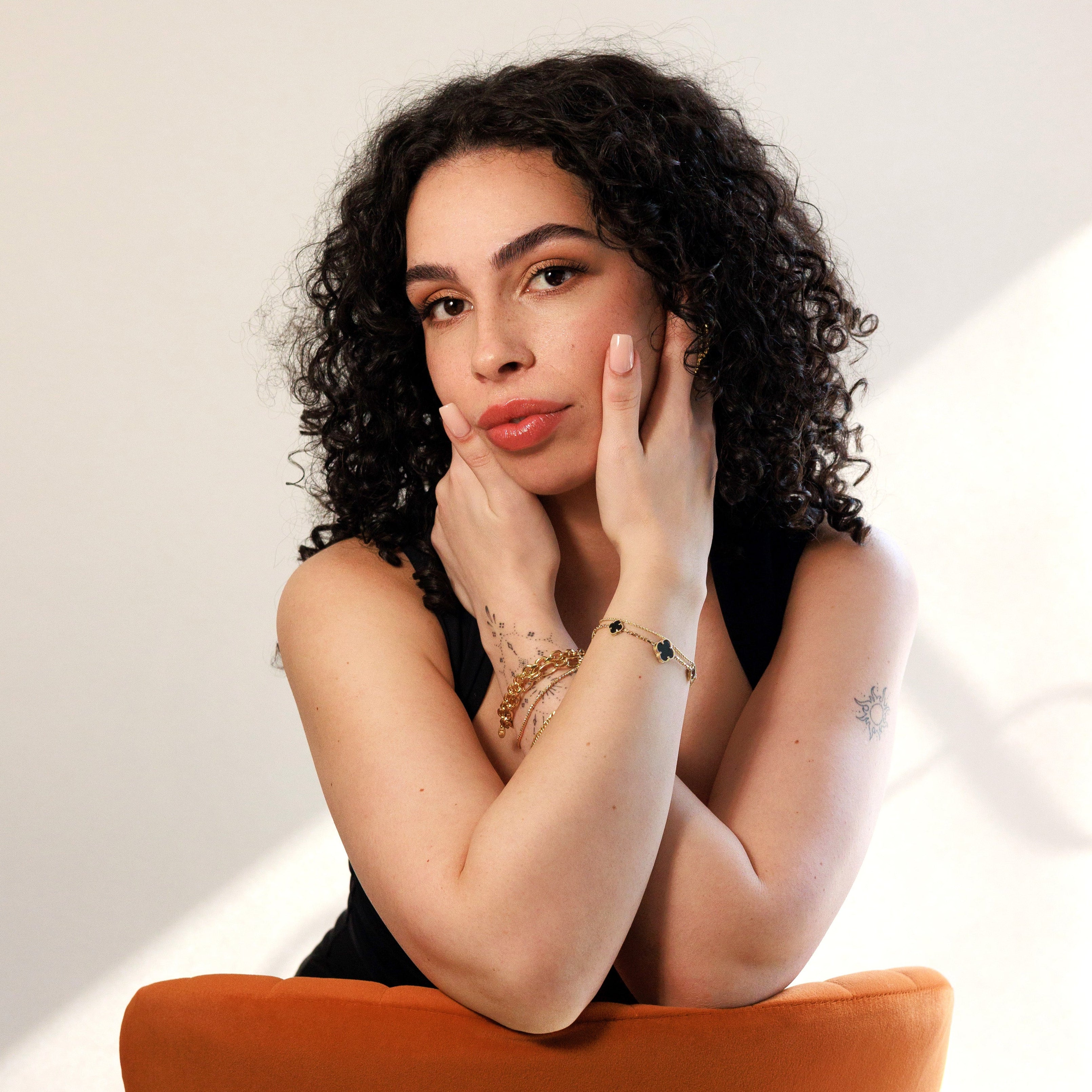 Woman with curly hair sitting on an orange chair against a white background